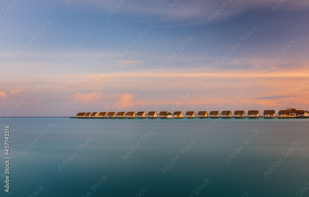 Island in ocean, overwater villas at the sunrise. Crossroads Maldives, july 2021. Long exposure picture