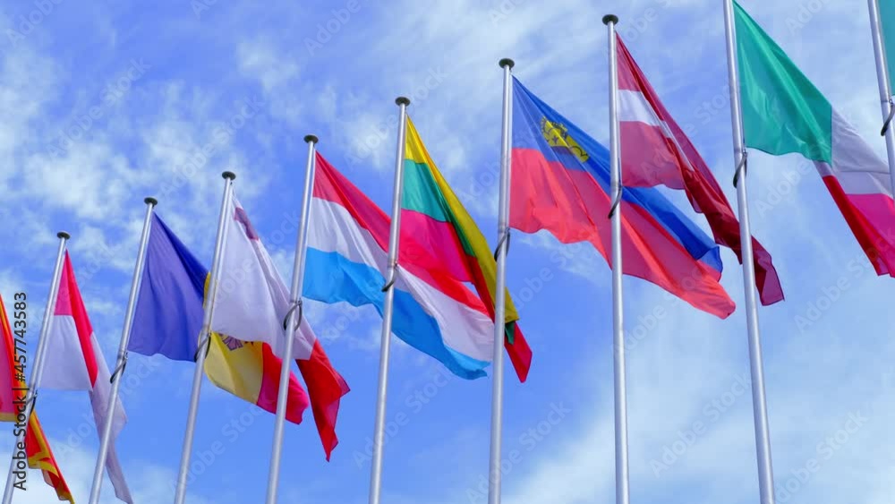 national flags of Europe and other countries on satin flutter in wind in blue sky near building of European Parliament, state symbols, concept of international cooperation, global business national flags of Europe and other countries on satin flutter in wind in blue sky near building of European Parliament, state symbols, concept of international cooperation, global business