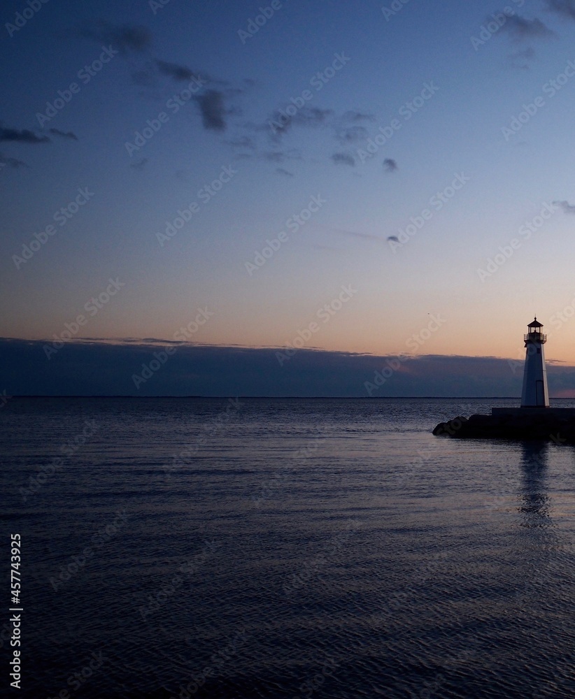 Lighthouse at sunset or twilight. Soft hint of orange color in clouds above the horizon and small lighthouse almost in silhouette at right.  Great South Bay, Long Island, New York State.  Vertical.