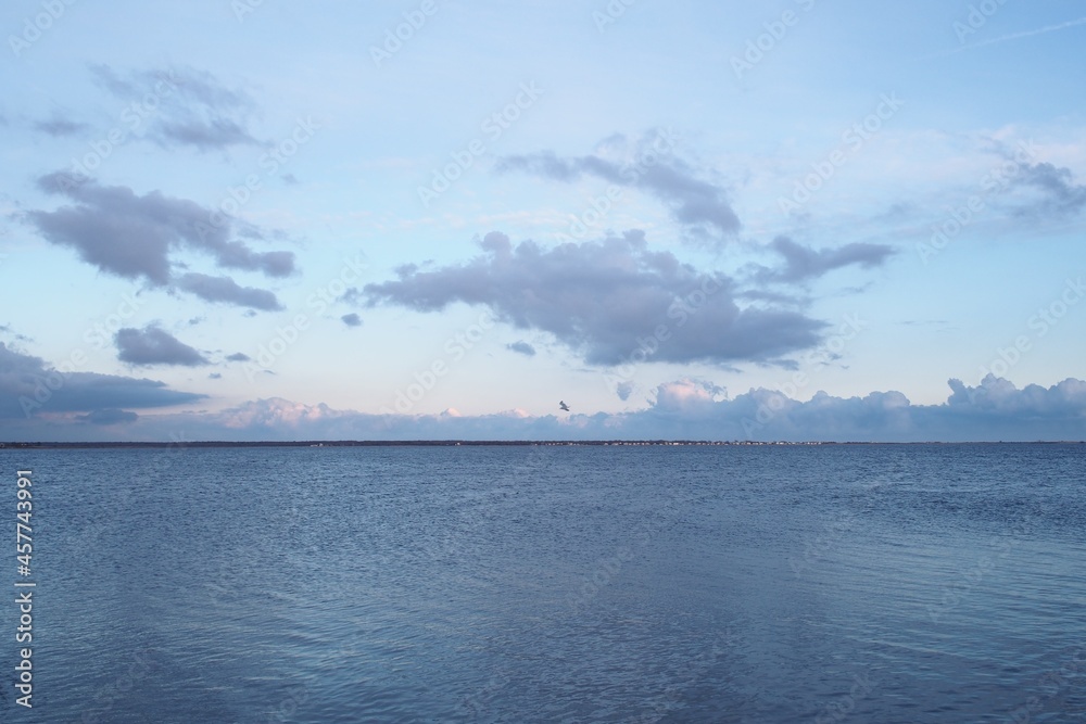 Near sunset, over bay, with slight current but otherwise calm water, pastel colored moody clouds sky over horizon. With copy space. Great South Bay, Long Island, New York.