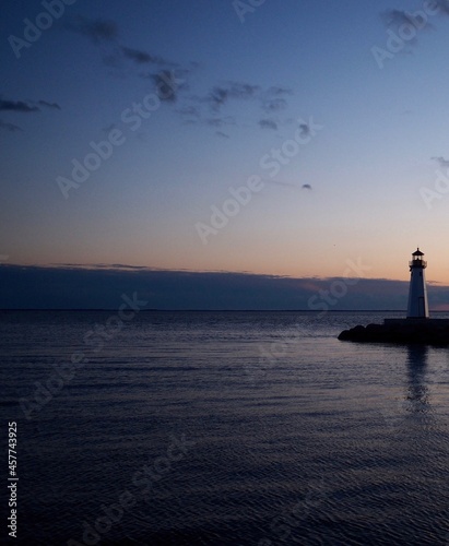 Lighthouse at sunset or twilight. Soft hint of orange color in clouds above the horizon and small lighthouse almost in silhouette at right. Great South Bay, Long Island, New York State. Vertical.