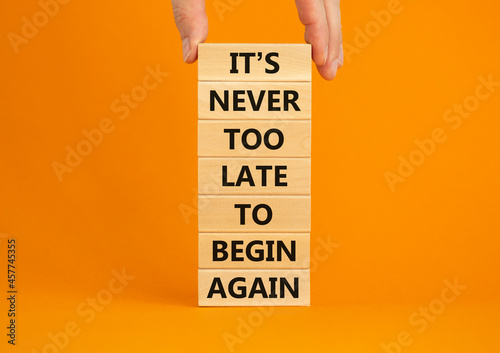 Begin again symbol. Wooden blocks with words 'It is never too late to begin again'. Businessman hand. Beautiful orange background, copy space. Business and It is never too late to begin again concept. photo