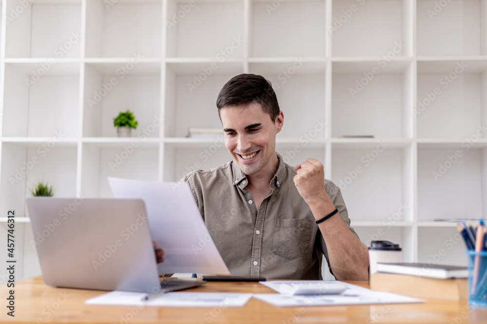 Young businessman sits in his office with a laptop, he looks delighted as he reads the documents that the company is profitable, he is a young businessman who is skilled in running the company to grow Young businessman sits in his office with a laptop, he looks delighted as he reads the documents that the company is profitable, he is a young businessman who is skilled in running the company to grow