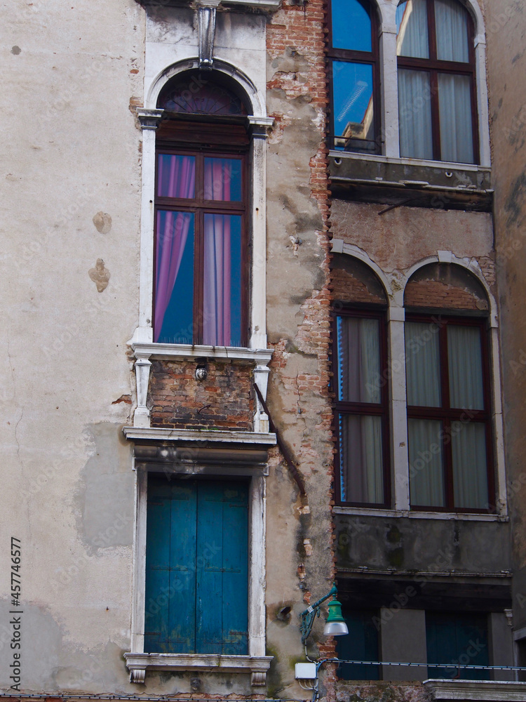 Venice, Italy - Narrow windows of two neighboring buildings, hint of purple curtains, damaged walls, seen from back alley
