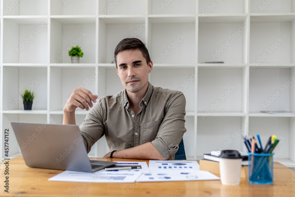 Young businessman sitting in office with laptop and financial documents showing chart data, young businessman founding startup company, managing a new business to grow by leaps and bounds.
