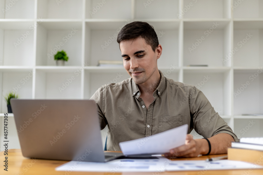 A young businessman sitting in the office working with a laptop, he is checking financial documents, he founded a startup, he is a young entrepreneur who has the skills to run a growing company. A young businessman sitting in the office working with a laptop, he is checking financial documents, he founded a startup, he is a young entrepreneur who has the skills to run a growing company.