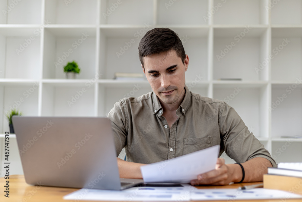 A young businessman sitting in the office working with a laptop, he is checking financial documents, he founded a startup, he is a young entrepreneur who has the skills to run a growing company. A young businessman sitting in the office working with a laptop, he is checking financial documents, he founded a startup, he is a young entrepreneur who has the skills to run a growing company.
