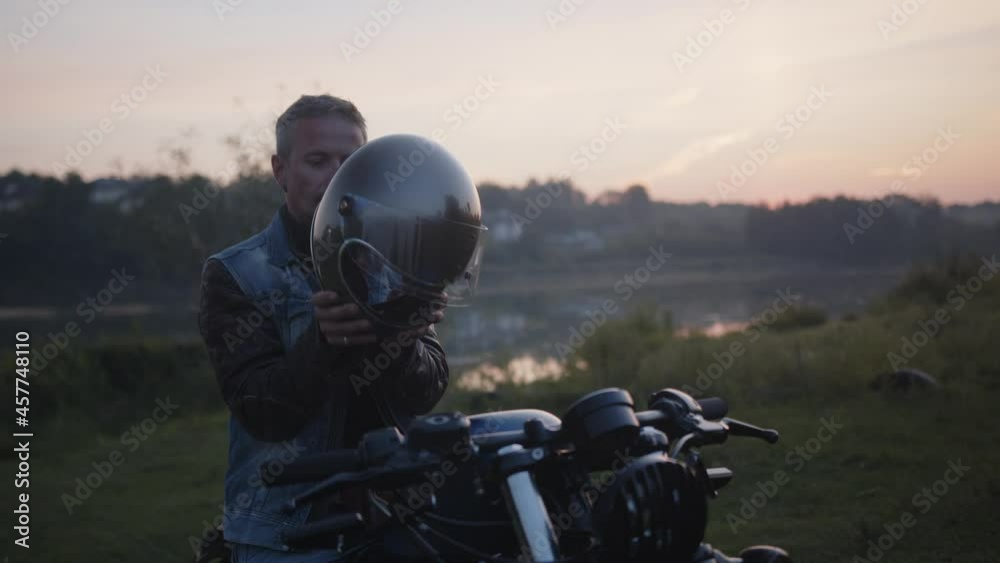 A handsome rider sitting on his motorcycle putting his silver motorcycle helmet on. A handsome rider sitting on his motorcycle putting his silver motorcycle helmet on.