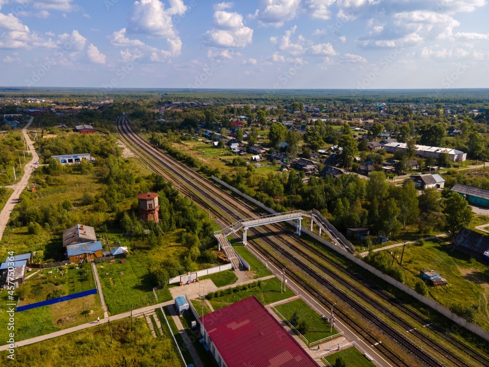 Railroad between trees and houses under cloudy blue sky