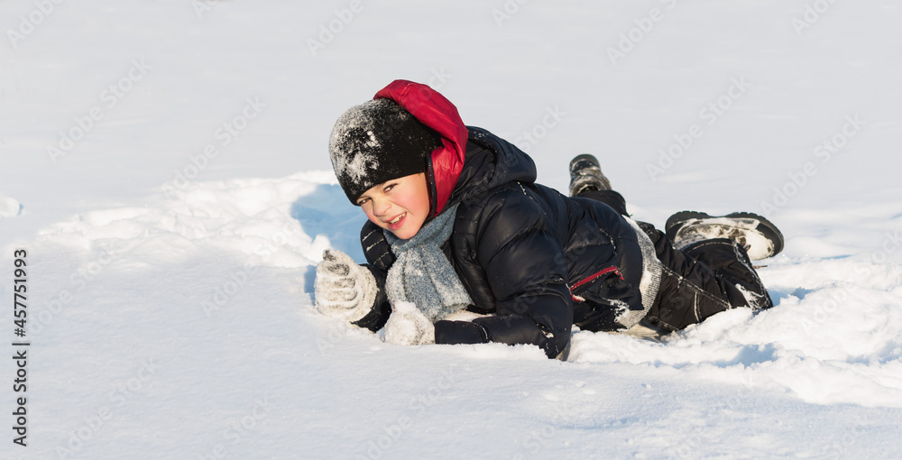 A little boy plays in the snow in winter