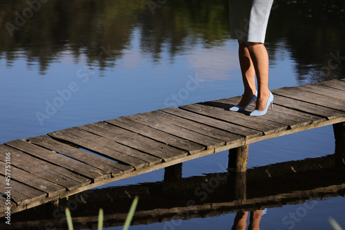 Fototapeta Naklejka Na Ścianę i Meble -  cropped photo of female legs walking on a wooden pier on the river