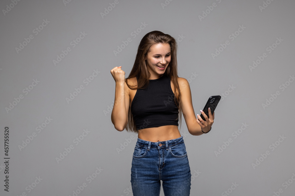 Portrait of a satisfied young woman holding mobile phone and celebrating isolated over gray background Portrait of a satisfied young woman holding mobile phone and celebrating isolated over gray background