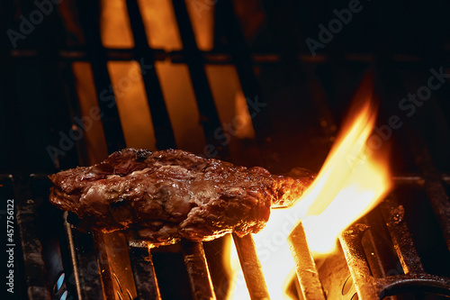 pedaço de carne assando na grelha de uma churrasqueira com labaredas subindo 