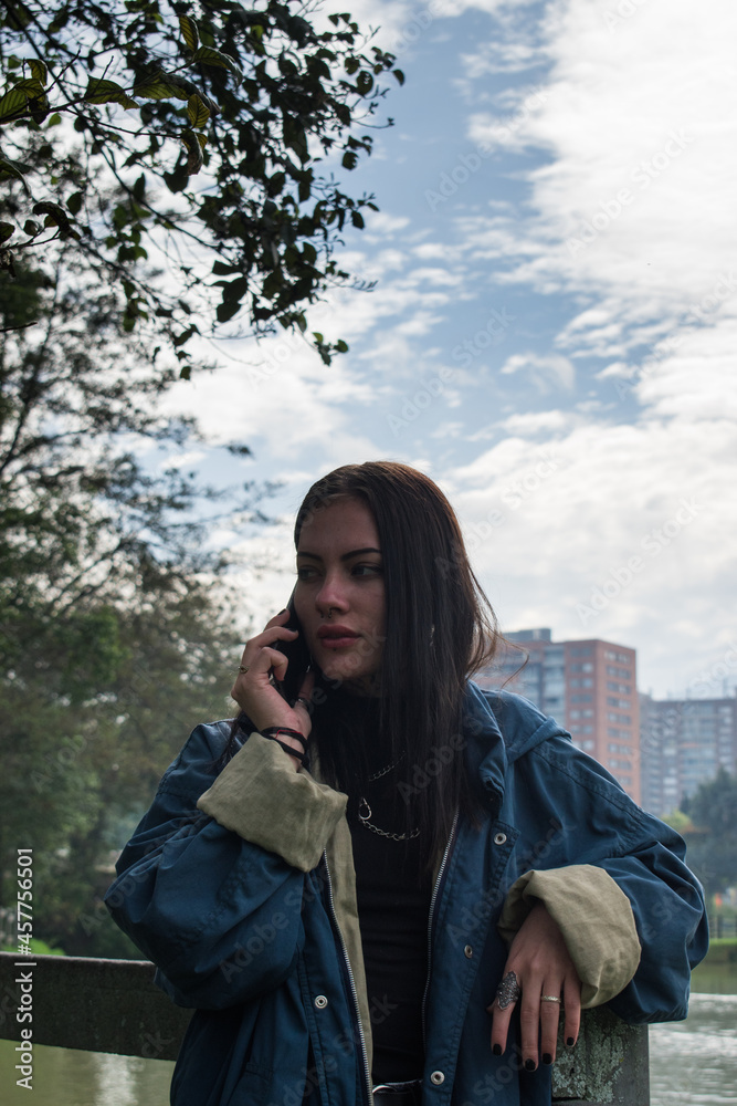 Young caucasian woman dressed in blue talking with her smartphone next to lake in a green park Young caucasian woman dressed in blue talking with her smartphone next to lake in a green park