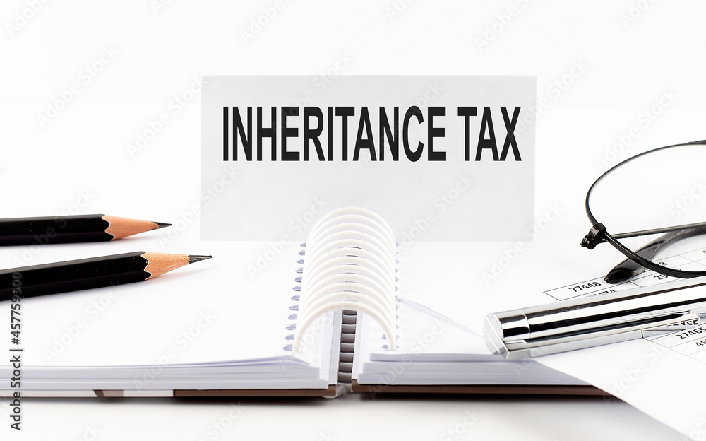 Text INHERITANCE TAX on paper card,pen, pencils, glasses,financial documentation on table - business concept