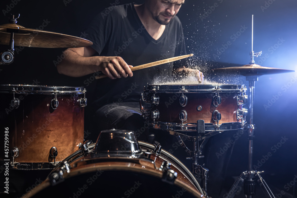 Fototapeta premium A male drummer plays snare drum with drumsticks in a dark room.