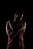 Side lit muscular Caucasian man silhouette. Athlete in red shirt posing against black background.
