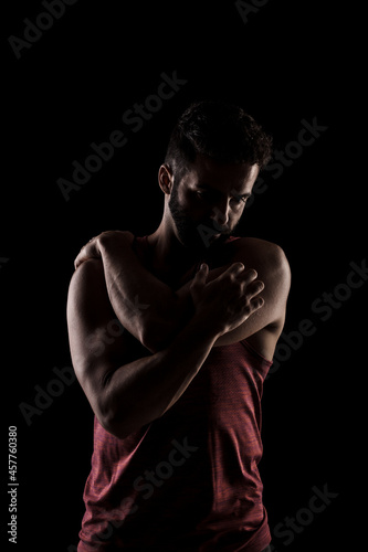 Side lit muscular Caucasian man silhouette. Athlete in red shirt posing against black background. © Nikola Spasenoski