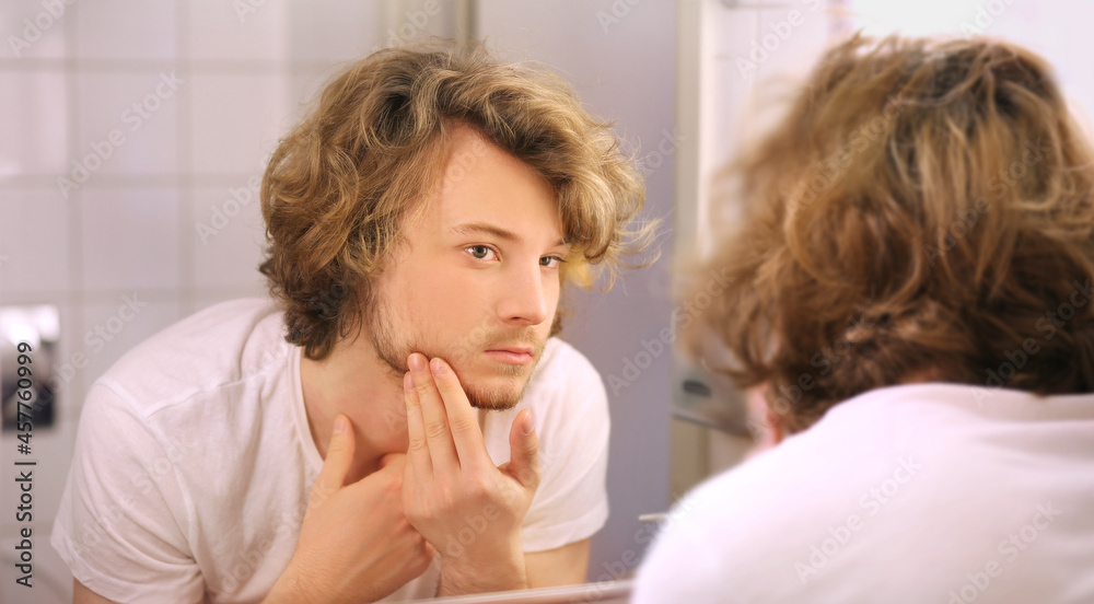 young man looking in the mirror,combing his hair,looking at problems on face young man looking in the mirror,combing his hair,looking at problems on face