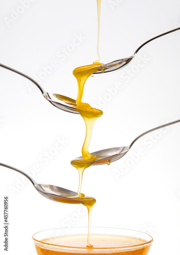 Fresh flower honey drips from a spoon into a spoon on a white background. Organic vitamin food.