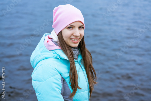 Happy tourist woman on the bank of the river in autumn in warm clothes. Tourists enjoy their vacation, winter season. Romantic look and travel concept. A joyful mood in a caucasian girl © Екатерина Переславце