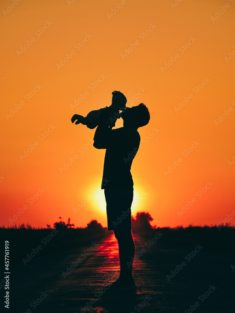The silhouette of the father holds and kisses his child at sunset