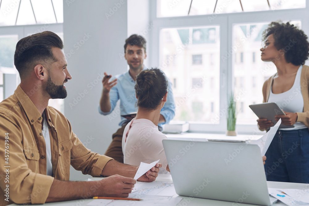 Group of modern young people in smart casual wear discussing business while having meeting in office Group of modern young people in smart casual wear discussing business while having meeting in office