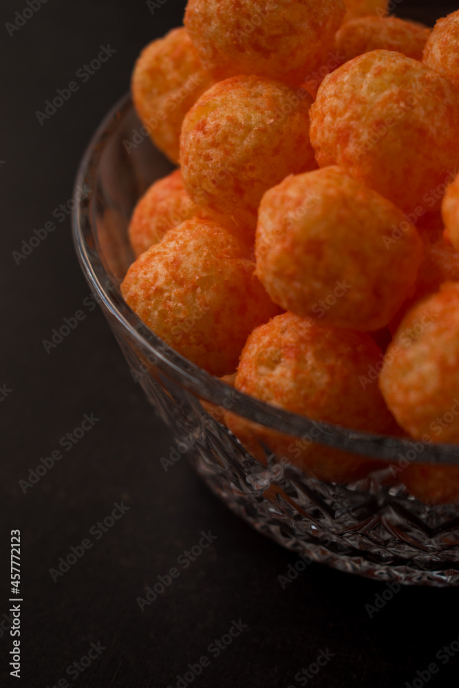 Cheese snack from a glass pot with cheese sticks and cheese balls on a black wooden table Cheese snack from a glass pot with cheese sticks and cheese balls on a black wooden table