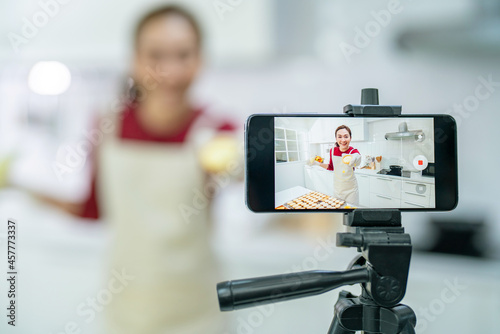 Asian woman bakery shop owner using smartphone with internet presentation sweet dessert bakery on social media in the kitchen. Small business entrepreneur and online marketing food delivery concept