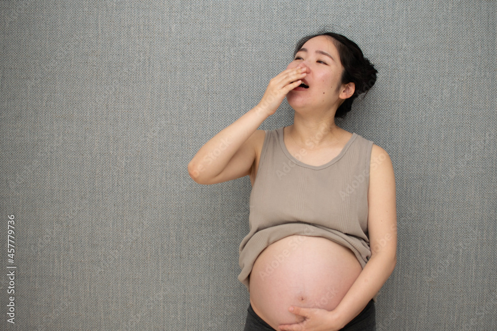 A young pregnant Asian woman yawning in front of wall