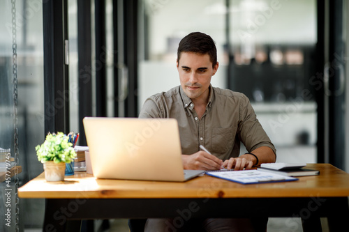 Young handsome man or businessman working on laptop computer in modern office.doing finances,accounting analysis,report,data and pointing graph Freelance education and technology concept.