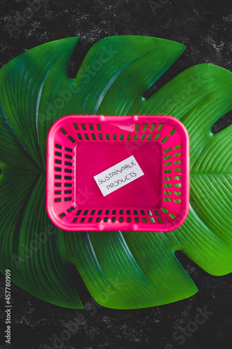 sustainable products and consumer behaviour, empty pink shopping basket with text on top of tropical green leaf