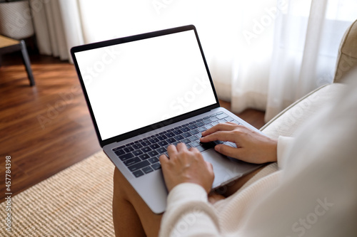 Mockup image of a woman working and typing on laptop computer with blank screen while sitting on a sofa at home