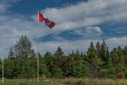 Canadian Flag on a pole with beautiful blue and cloudy sky in a rural environment