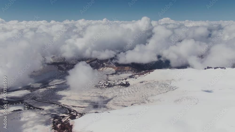 A view from a snow-covered mountain peak to a valley covered with cumulus clouds A view from a snow-covered mountain peak to a valley covered with cumulus clouds