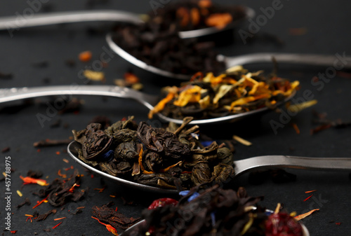 Virious kinds of tea in tea spoons on black table close-up, Assortment of teas. Black , green and fruit tea, dry tea leaves