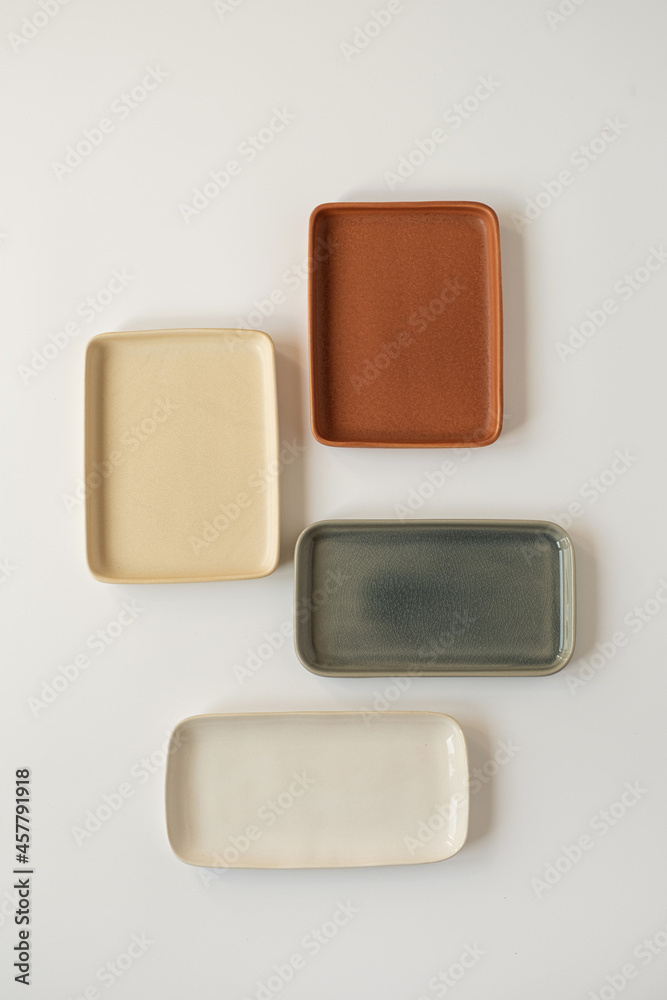 Empty blank ceramic round bowl and square plates on white background. Flat lay, top view of traditional handcrafted homemade kitchenware concept Empty blank ceramic round bowl and square plates on white background. Flat lay, top view of traditional handcrafted homemade kitchenware concept