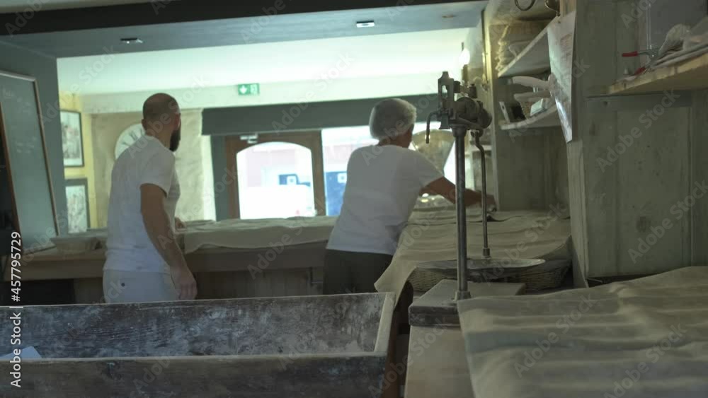 mid shot of two bakers preparing traditional french bread, kneading dough, placing it in osier basket, and covering with linen blanket mid shot of two bakers preparing traditional french bread, kneading dough, placing it in osier basket, and covering with linen blanket
