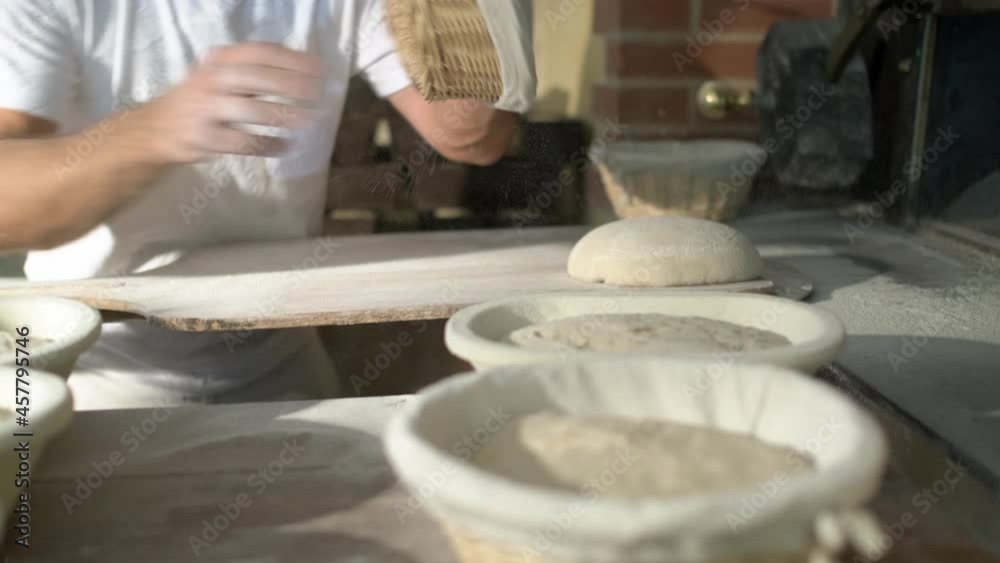 side shot, a baker flouring, cuting and puting bread loaf in a traditional stone oven, using baker’s peel side shot, a baker flouring, cuting and puting bread loaf in a traditional stone oven, using baker’s peel