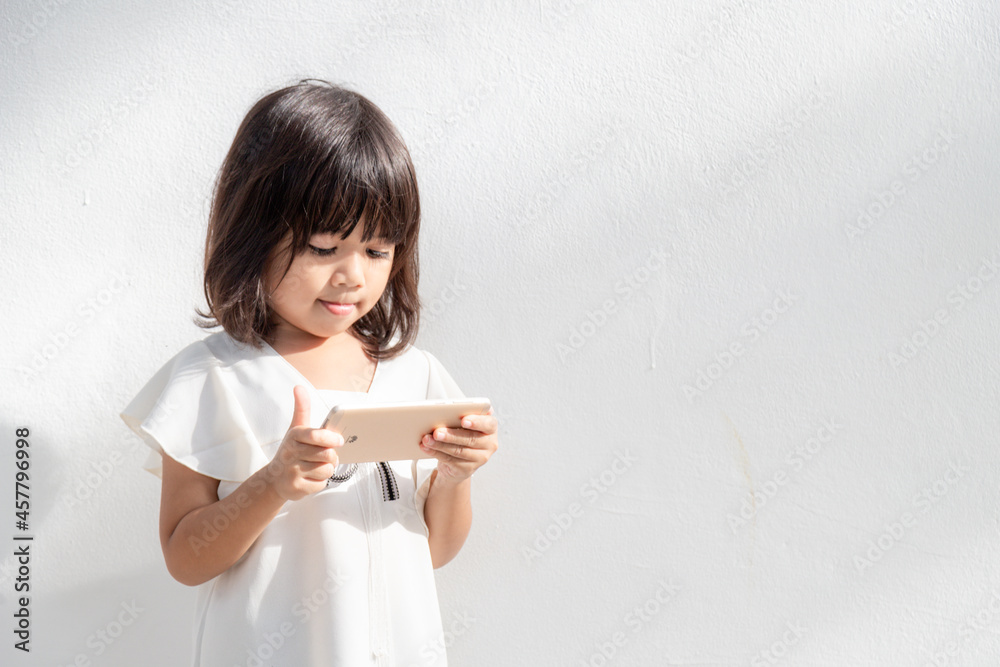 A little girl is concentrated on the phone, look at the smartphone, technology concept for children, profile view, isolated on white background, copy space A little girl is concentrated on the phone, look at the smartphone, technology concept for children, profile view, isolated on white background, copy space