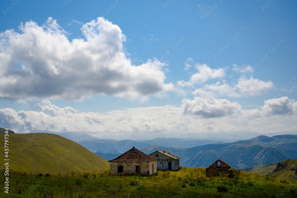 abandoned village of three tile roof houses left by people in highland green mountains under blue cloudy sky