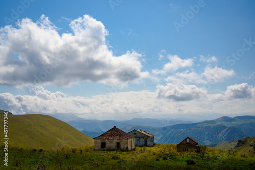 abandoned village of three tile roof houses left by people in highland green mountains under blue cloudy sky