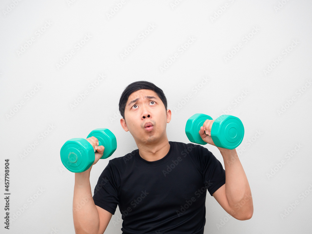 Asian man holding drumbbell feeling amazed and looking up copy space white background Asian man holding drumbbell feeling amazed and looking up copy space white background