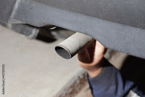 Test the exhaust system of the used car - a man's hand checks the exhaust silencer pipe clamp fastening under the bottom of the vehicle photo