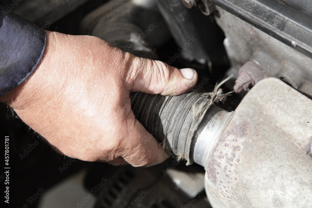 Obraz premium Air heating for an automobile engine intake in winter - a man's hand puts a nozzle on the exhaust manifold heat shield closeup, seasonal vehicle maintenance service