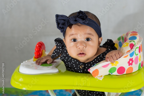 Southeast asian baby girl learning to walk at home with the help of baby walker. closeup of a baby girl sitting on baby walk. 