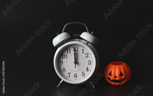 white vintage alarm clock show 12 o'clock  with halloween pumpkin on black background. Halloween hoiday party. photo