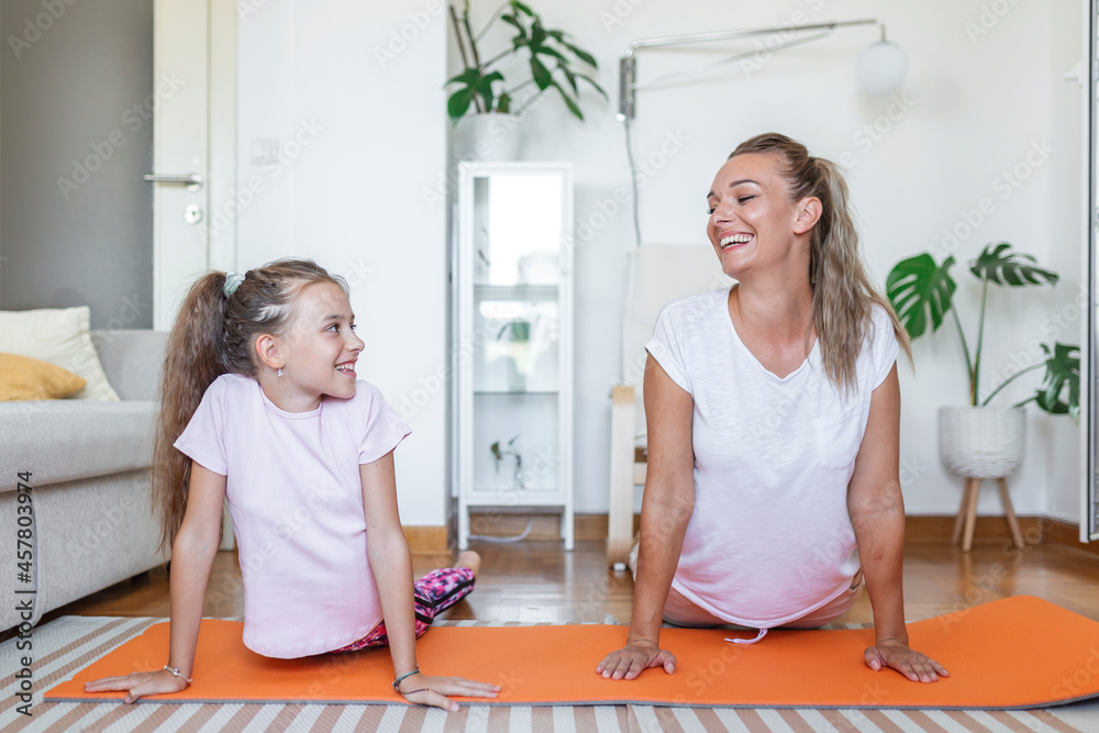 Obraz premium Cheerful fit female and little daughter doing lunges exercises while training together in front of laptop in modern apartment. family mother and child daughter are engaged in fitness