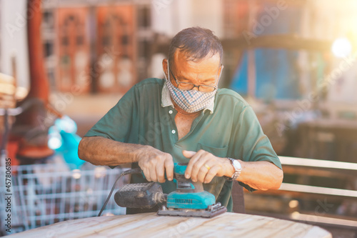 Old man of carpenter working with machine on table