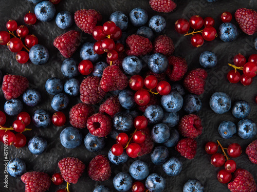  Raspberries  red currants and blueberries on a dark plate in a low key. Close-up. View from above. flat lay.